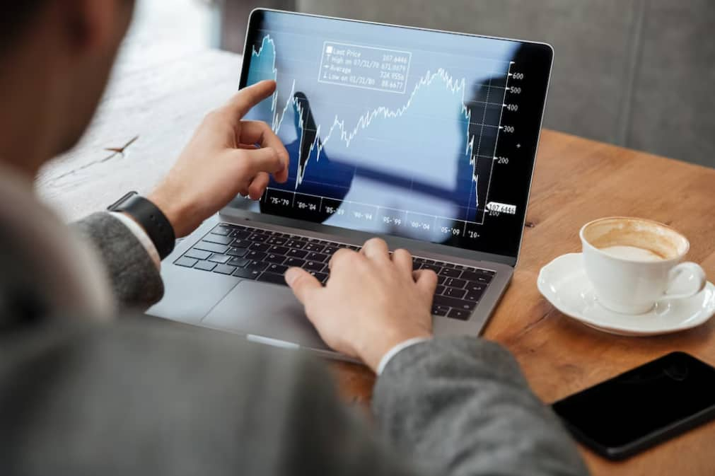 A person analyzing financial charts on a laptop with a cup of coffee nearby