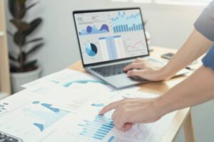 A person analyzes financial charts on a laptop and printouts