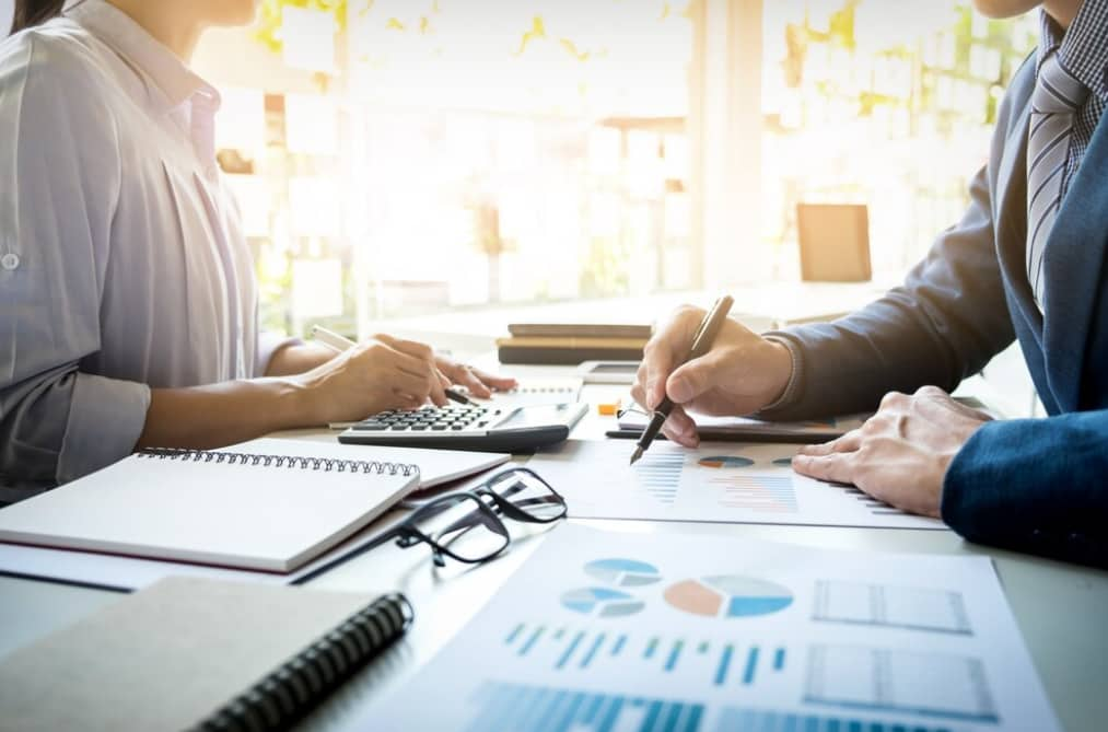 Two professionals discuss over financial documents on a desk