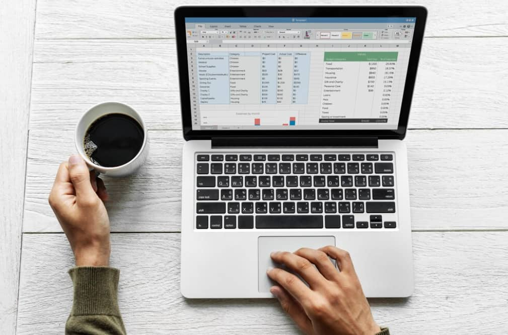 Close-up of a laptop with a budget spreadsheet next to a cup of coffee