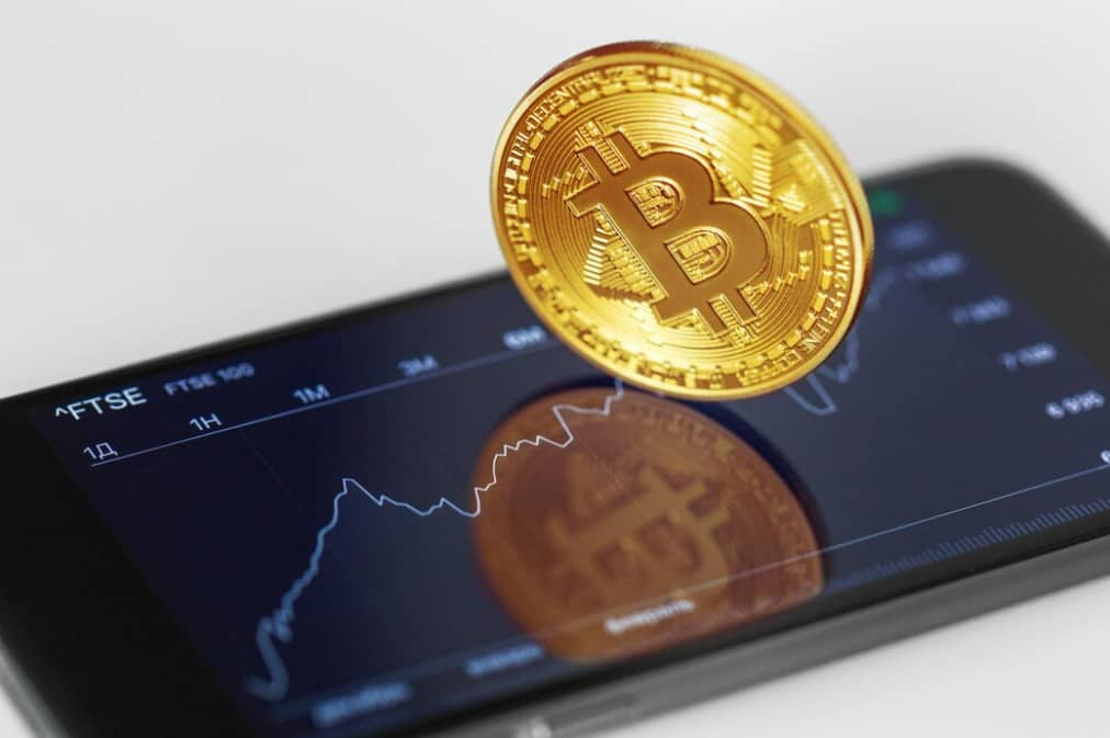 A bitcoin atop a smartphone displaying a financial chart